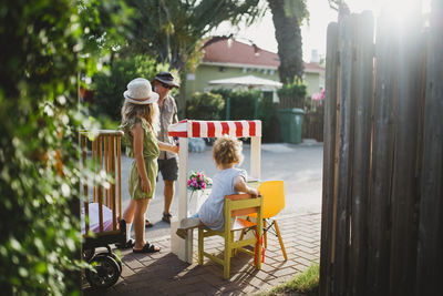 Two sisters playing with market stand selling flowers to a man