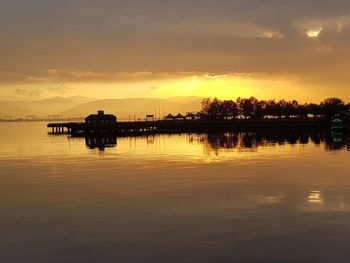 Silhouette built structure by river against sky during sunset