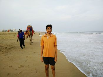 Portrait of young man standing at beach against cloudy sky