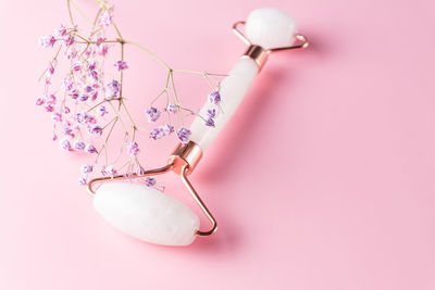 Face roller and gypsophila flower on pink background. massage tool for facial skin care, spa beauty