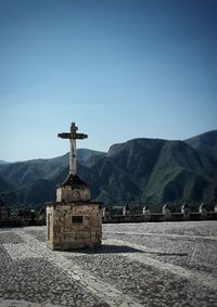 Cross on building by mountains against clear blue sky