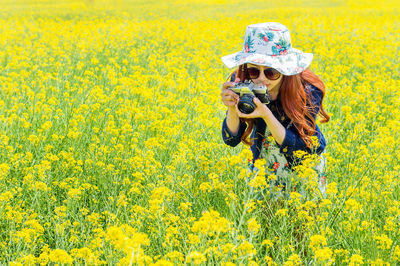 Woman photographing with camera at rape field