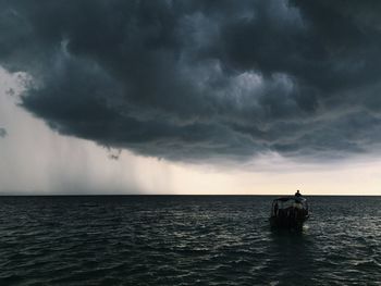 Man sailing boat in ocean against storm clouds