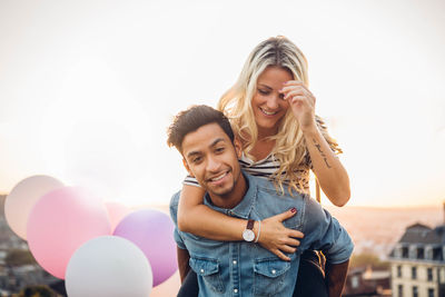 Couple standing with balloons against sky