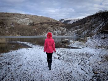 Woman with red coat standing near a lake during winter