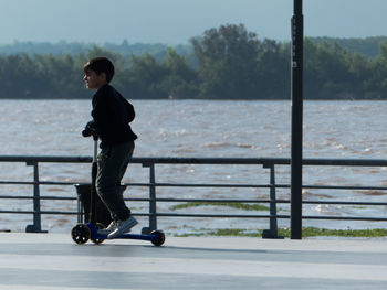 Side view of boy with push scooter by railing