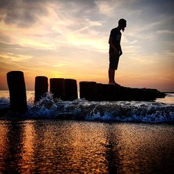 Silhouette man standing on rock by sea against sky during sunset