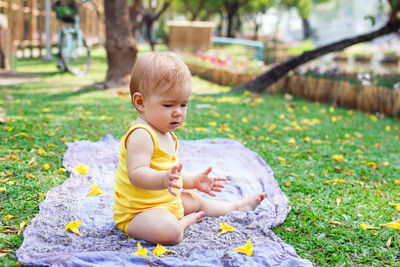 Adorable little caucasian girl in yellow dress is playing with yellow flowers on a plaid.