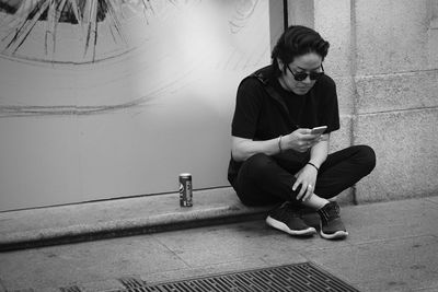 Young woman using mobile phone while sitting on wall