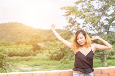 Beautiful young woman with arms raised against plants