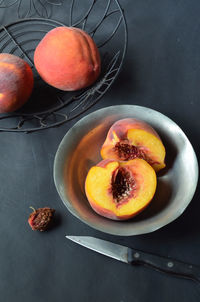 Halved peach in pewter bowl, wire basket with whole peaches, peach pit and knife