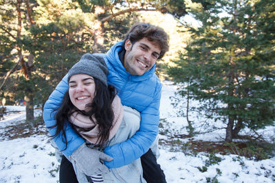 Smiling young woman giving piggyback to boyfriend on field during winter