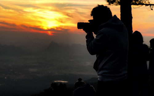 Silhouette man photographing with camera against sky during sunset