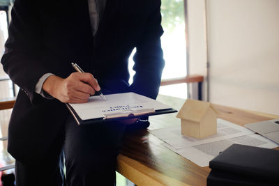 Midsection of insurance agent sitting on table at office while signing contract