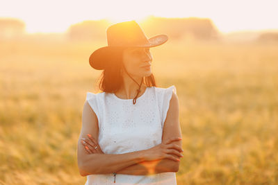 Side view of young woman standing on field against sky during sunset