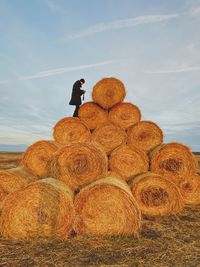 Man standing on hay bales over land against sky