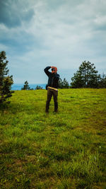 Man photographing while standing on grassy field against cloudy sky