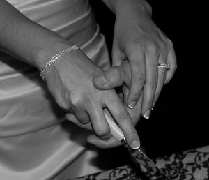 Midsection of bride and bridegroom cutting cake