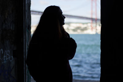 Rear view of silhouette woman standing on doorway by sea