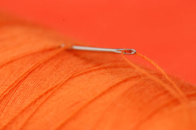 Close-up of orange thread spool with needle against orange background