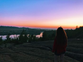 Rear view of woman standing on field against sky during sunset