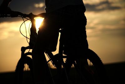 Low section of silhouette man riding bicycle against sky during sunset