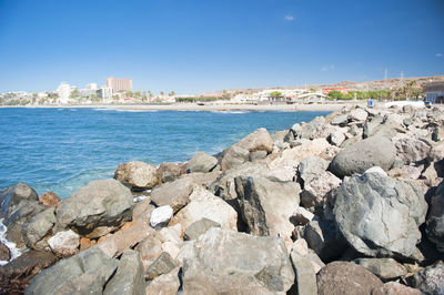Rocks by sea against clear blue sky
