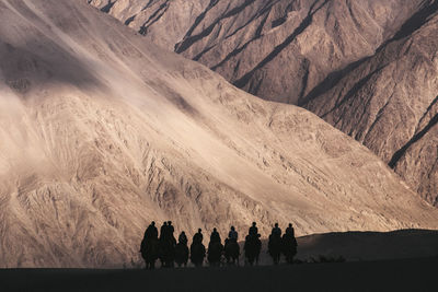 Silhouette people riding camels in desert against mountains