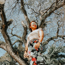 Low angle view of woman standing by tree against sky