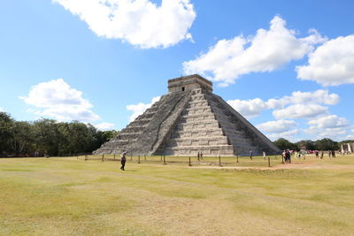 Tourists on field against cloudy sky