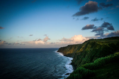 Grassy mountain by sea against sky at azores