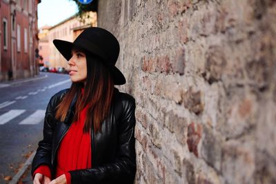 Woman looking away while standing by old brick wall