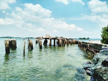 Wooden posts in sea against sky