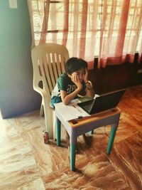 Boy with head in hands looking at laptop at home