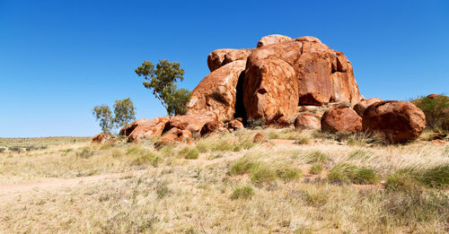 Rock formations on field against clear blue sky