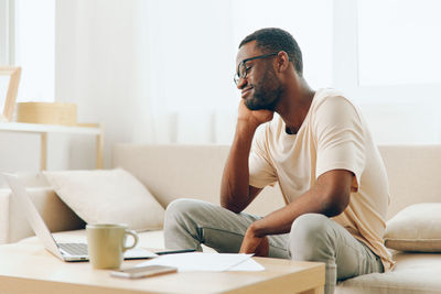 Young man using laptop while sitting on sofa at home