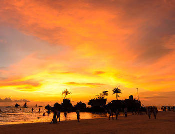 Silhouette people on beach against orange sky