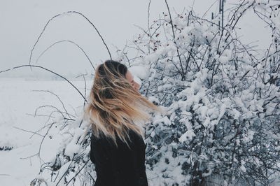 Side view of woman standing by snow covered plants