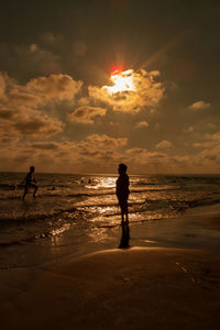 Silhouette man standing on beach against sky during sunset