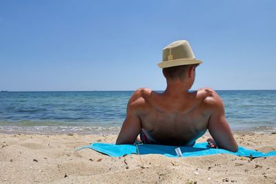 Shirtless man relaxing at beach against clear sky