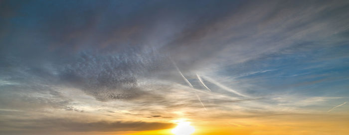 Low angle view of sunlight streaming through clouds during sunset