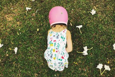 Rear view of girl wearing pink helmet while bending on grassy field