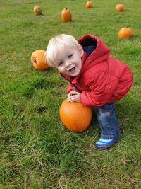 Full length of cheerful boy sanding with pumpkin on field