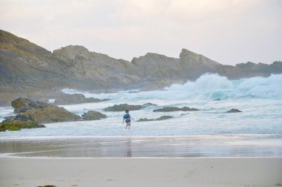 Boy on shore at beach against sky during sunset