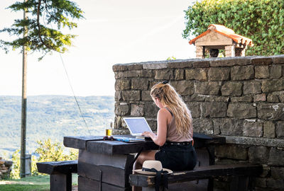 Young woman working on vacation, using laptop, outside.