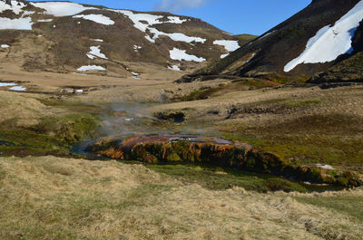 Steam rising from a hot spring river in a valley surrounded by mountains with snow.