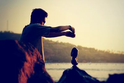 Side view of man standing on land against sky during sunset