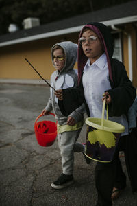 Full length of brothers dressed up as harry potter and owl walking on road with buckets during halloween