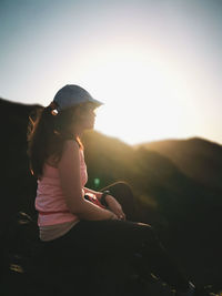 Side view of woman sitting against sky during sunset