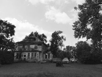 Abandoned building by trees on field against sky